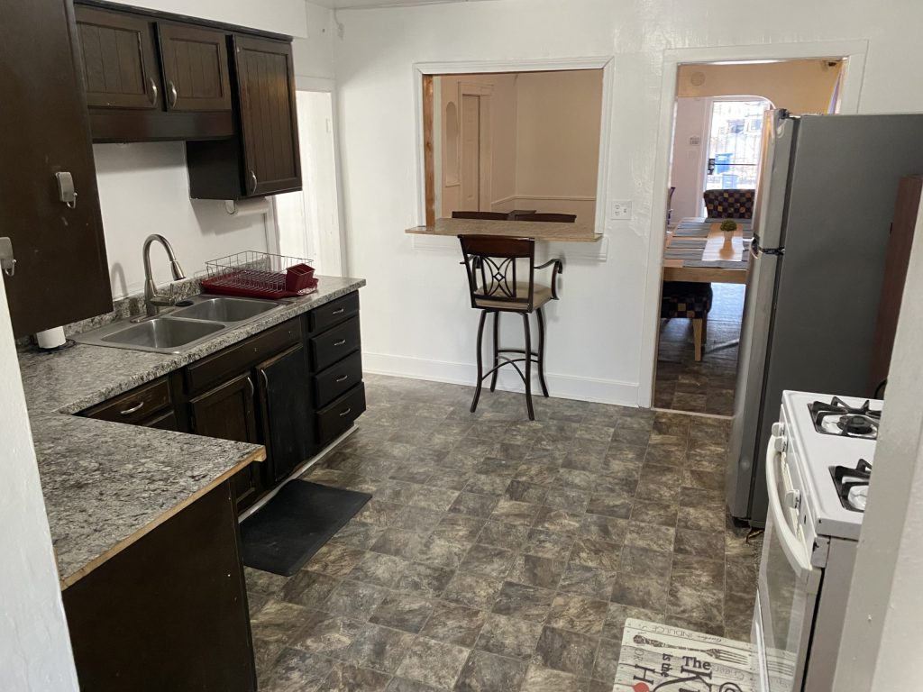 Kitchen with dark cabinets, a double sink, gas stove, and a pass-through window to a dining area with a table and chairs.